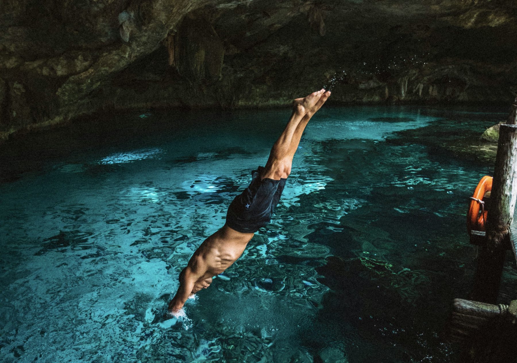 Een man duikend in helder blauw water in een grot in Mexico.