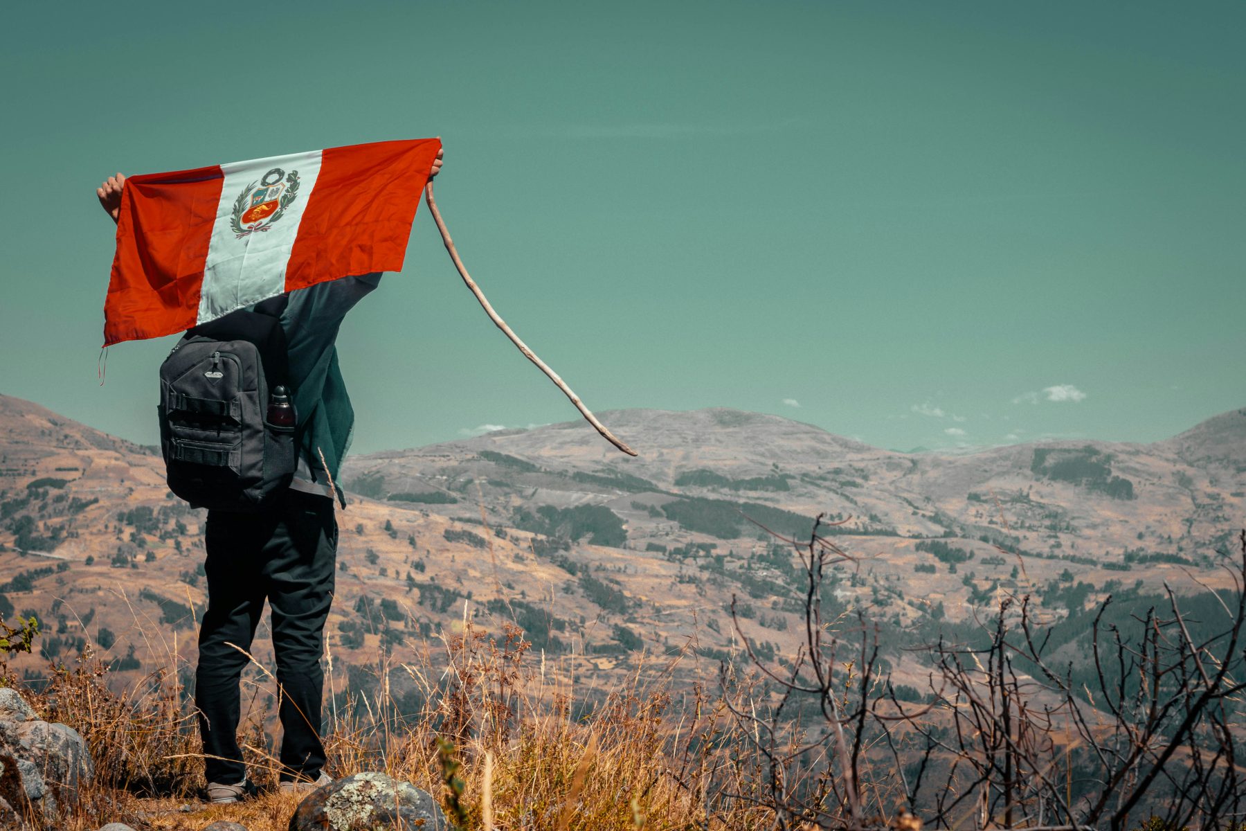 Een man die uitkijkt over een landschap in Peru, terwijl hij de Peruaanse vlag omhoog houdt.