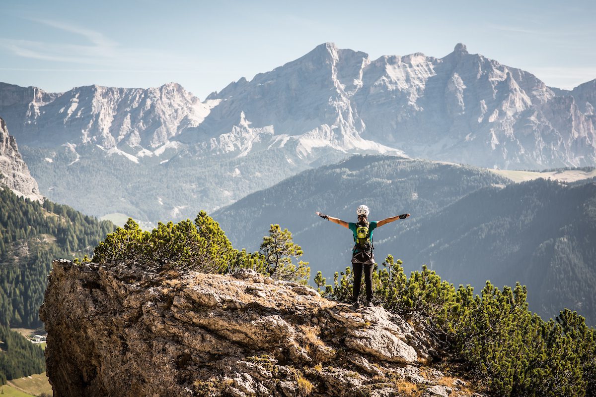 Een persoon staand op een gesteente uitkijkend over een bergachtig landschap in de Dolomieten.