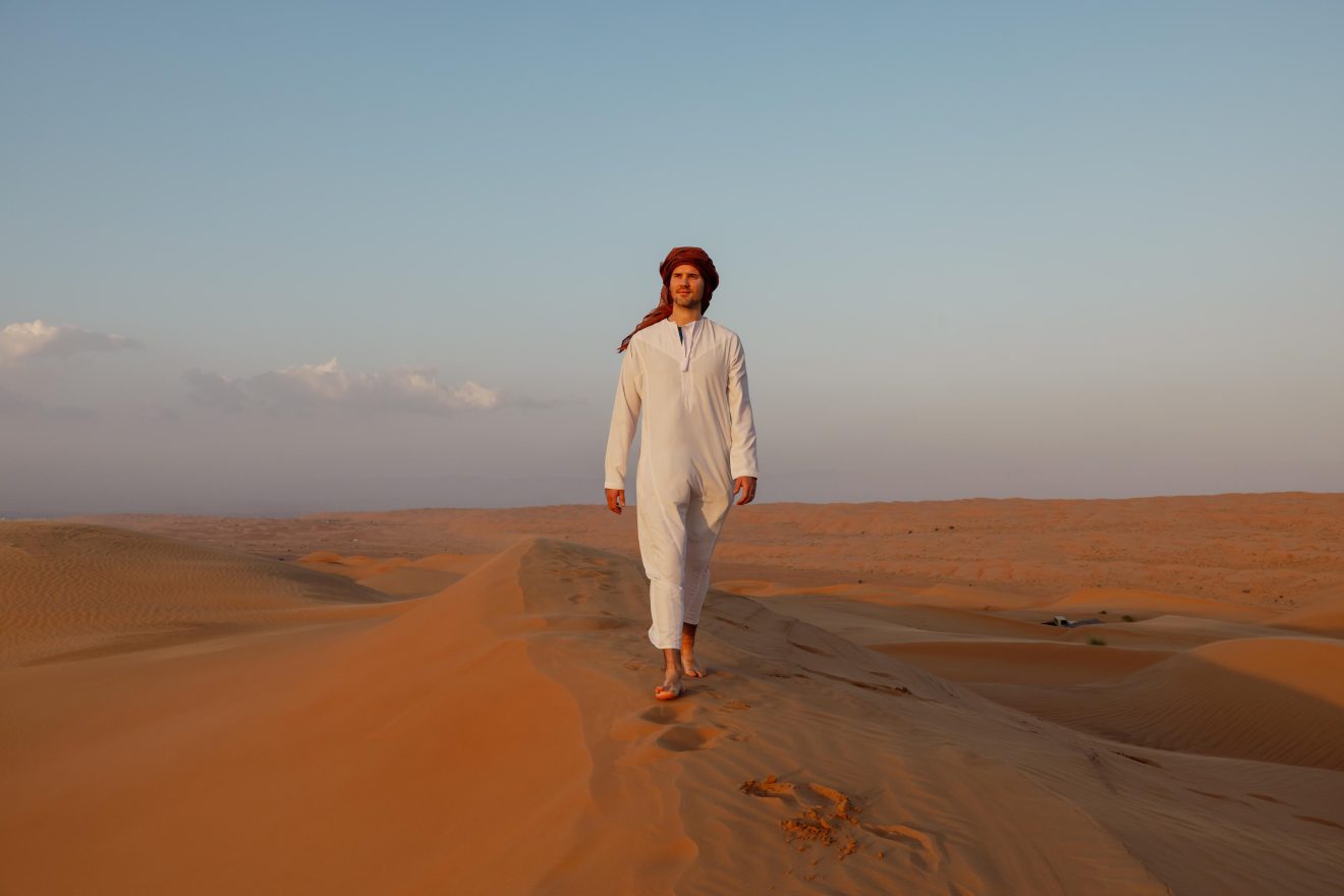 Persoon lopend door de woestijn in Oman, wat ook onderdeel is van Oman Nomads.