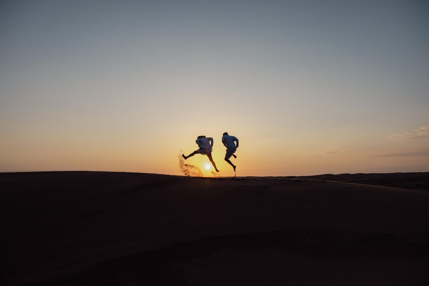 Twee personen in de woestijn in Oman tijdens zonsondergang.