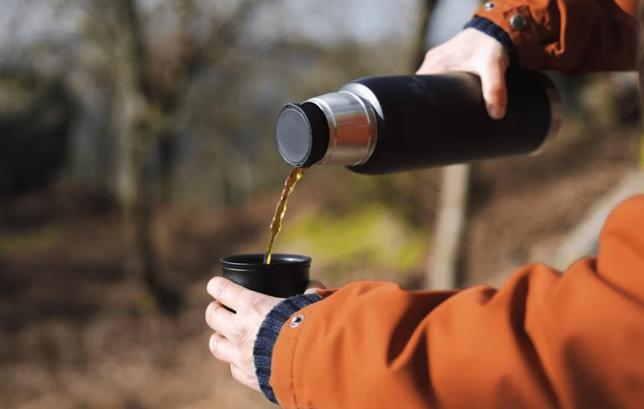 Een persoon die drinken uit een zwarte Stanley Thermosfles 'To-Go' schenkt in de bijbehorende drinkbeker.