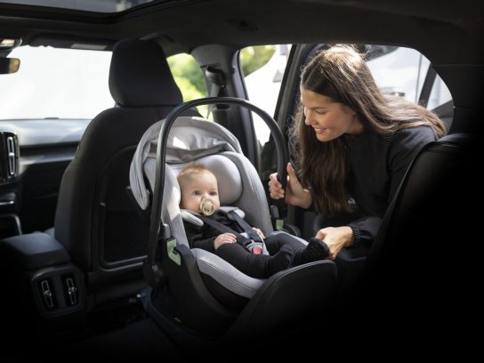 Een vrouw installeert een baby in een autostoeltje van Thule achterin een auto.