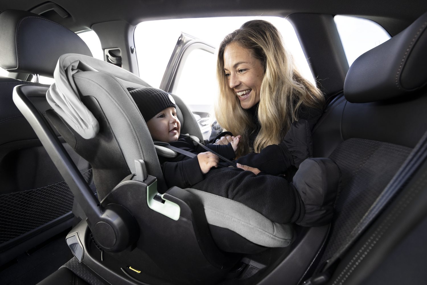 Een vrouw zit achterin de auto bij een kindje dat in een autostoeltje van Thule zit.