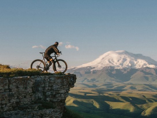 Een man op een fiets bij de rand van een klif met uitzicht op een bergachtig landschap.