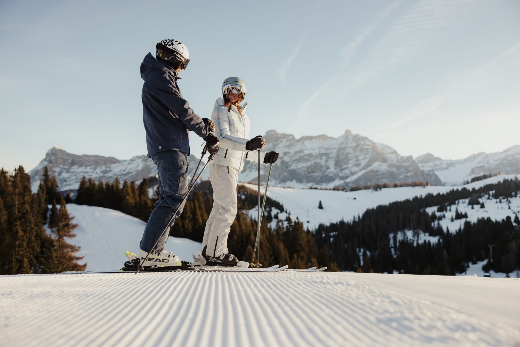 Twee mensen staan op ski's in de sneeuw met op de achtergrond bergen.