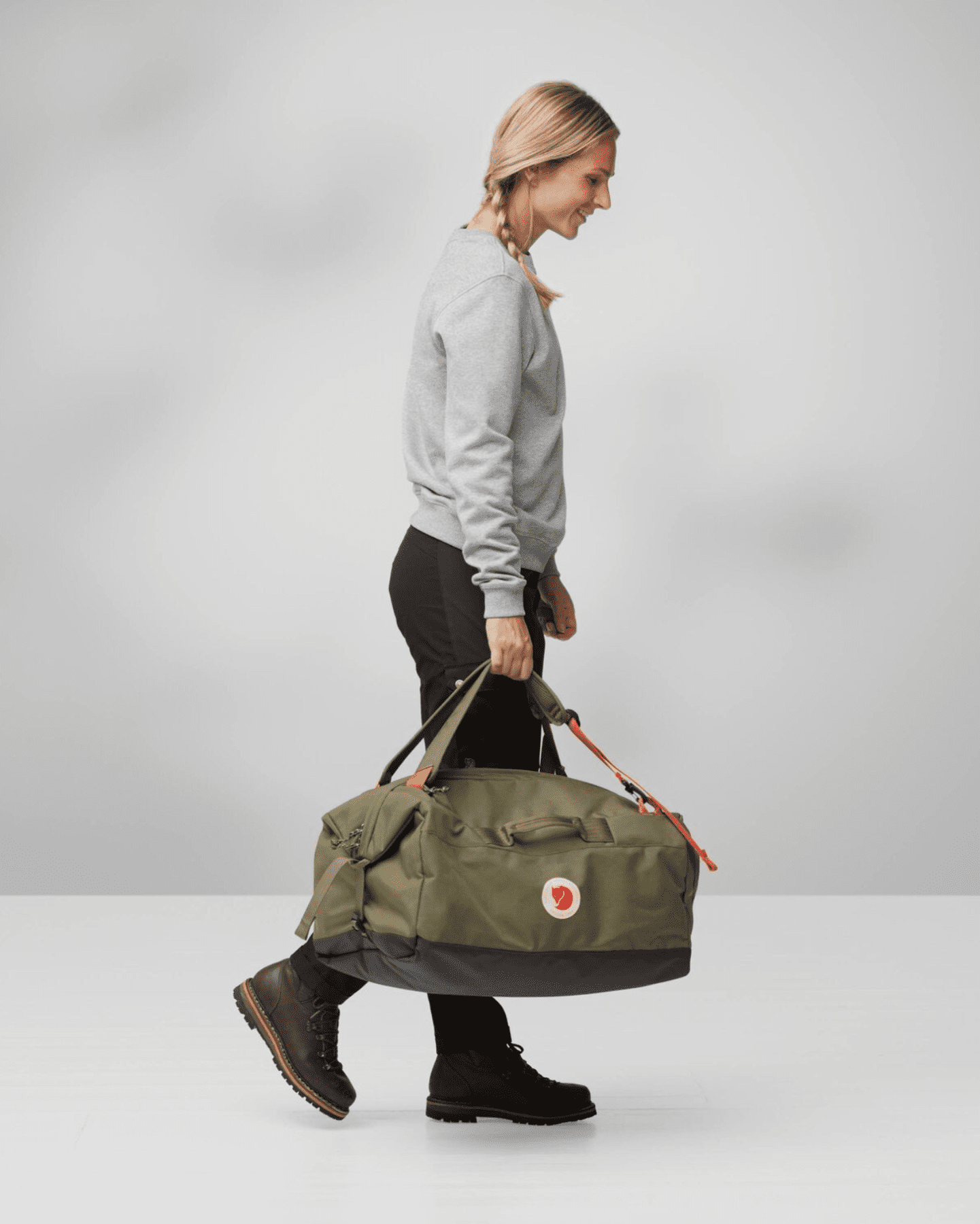 Een blonde vrouw draagt de groene Färden Duffel 50 uit de Färden reisduffel collectie in haar hand.