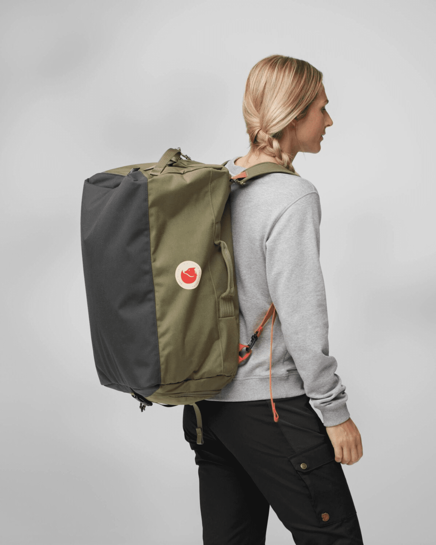 Een blonde vrouw draagt een groene tas van Fjällräven op haar rug.