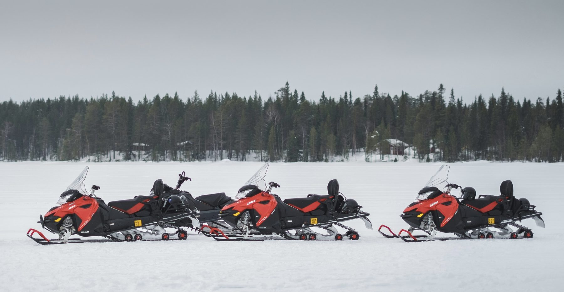 Vier sneeuwscooters midden in een sneeuwlandschap met bomen op de achtergrond.