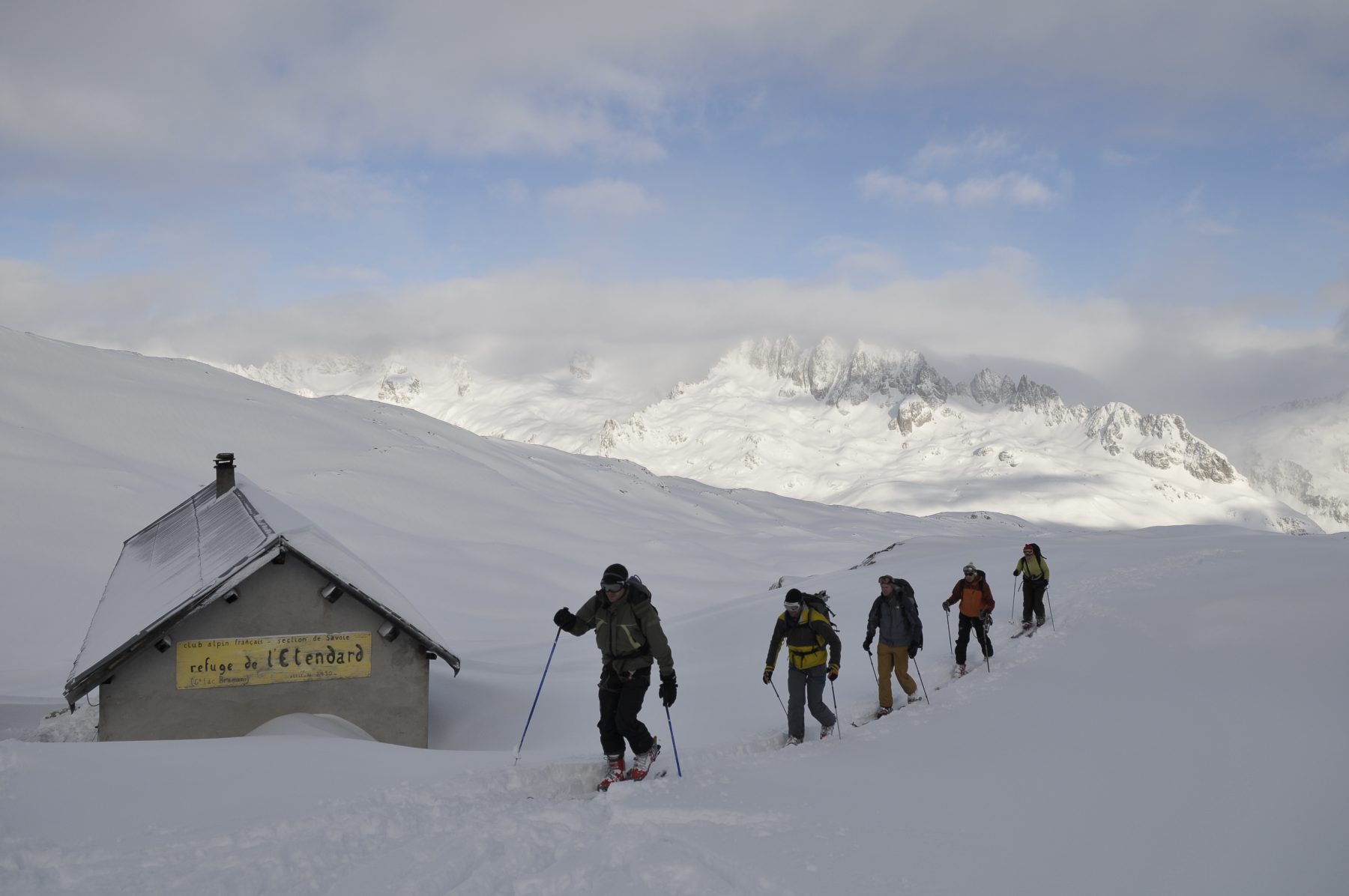 Vijf mensen komen tijdens het langlaufen door de besneeuwde bergen langs Refuge de l'Etendard; één van de berghutten in Isère.