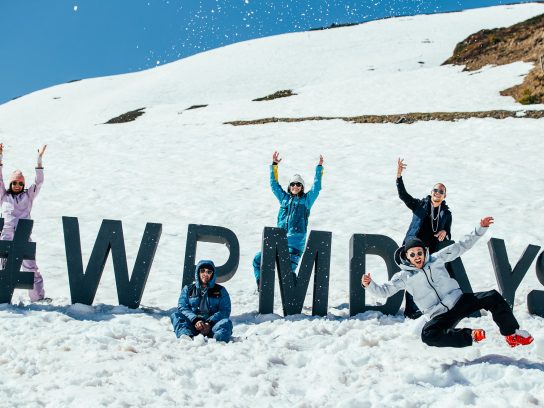 Mensen staan op een besneeuwde berg rondom grote letters waarmee '#WPMDAYS' is gespeld.