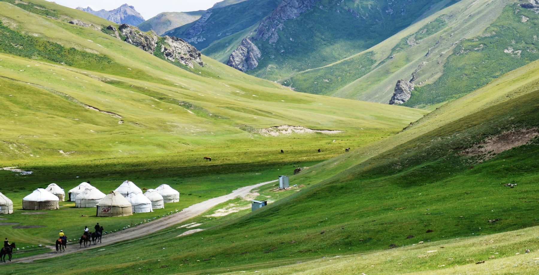 Een aantal mensen rijdend op een paard door een bergachtig landschap in Kirgizië.