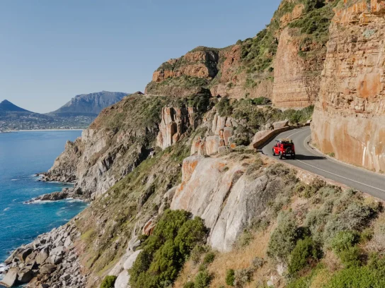 Een auto rijdt over een bergweg met uitzicht op de zee tijdens South Africa Nomads.