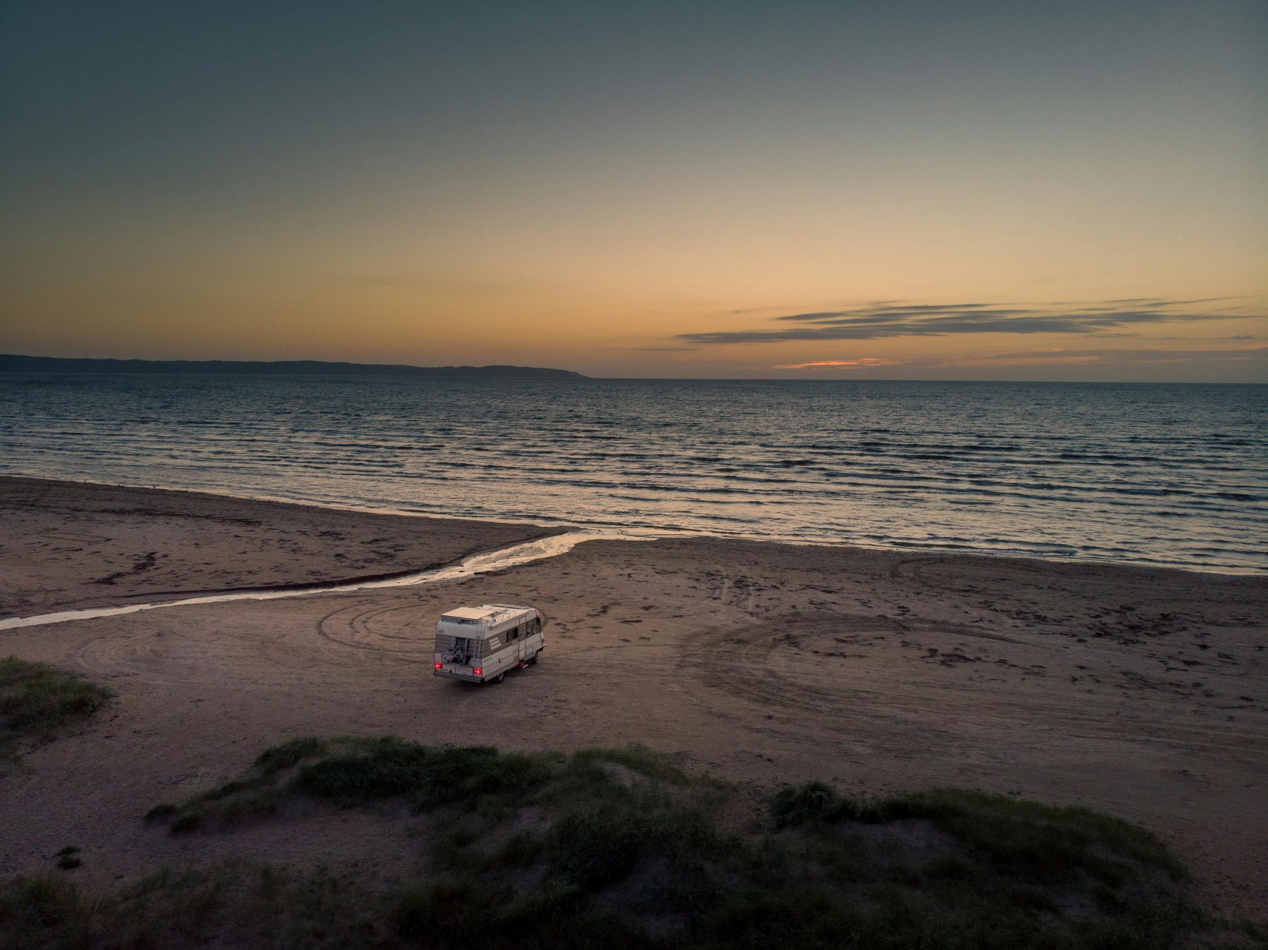 Een camper op een strand in Scandinavië tijdens zonsondergang.