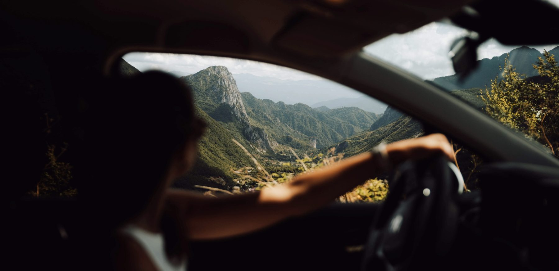 Een persoon zit in een auto en kijkt door het raam naar een bergachtig landschap in Albanië tijdens Albania Nomads.